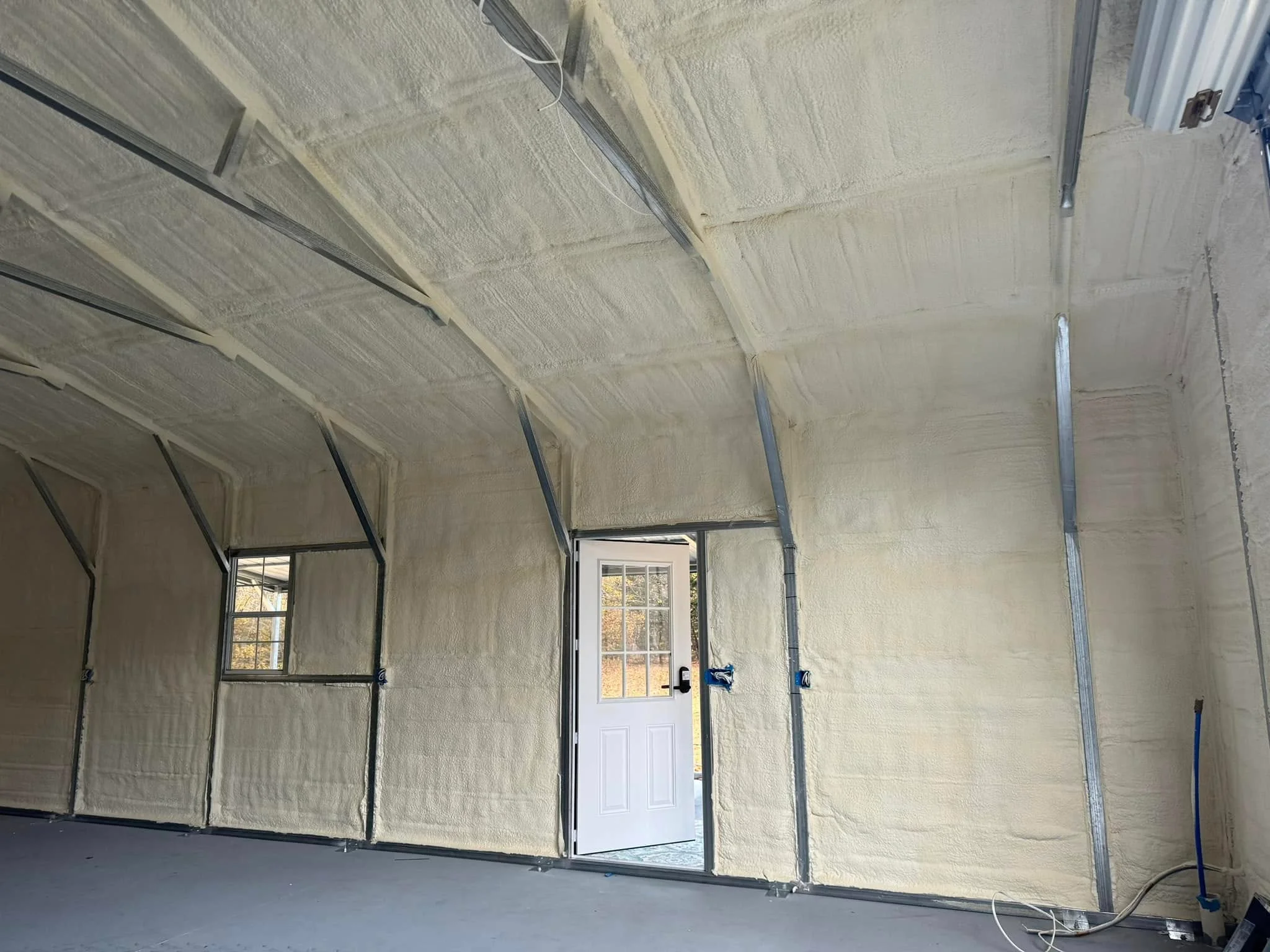 Interior of a metal building garage insulated with spray foam across the ceiling and walls, featuring a white door and window Insulation Company in Salisbury, MD
