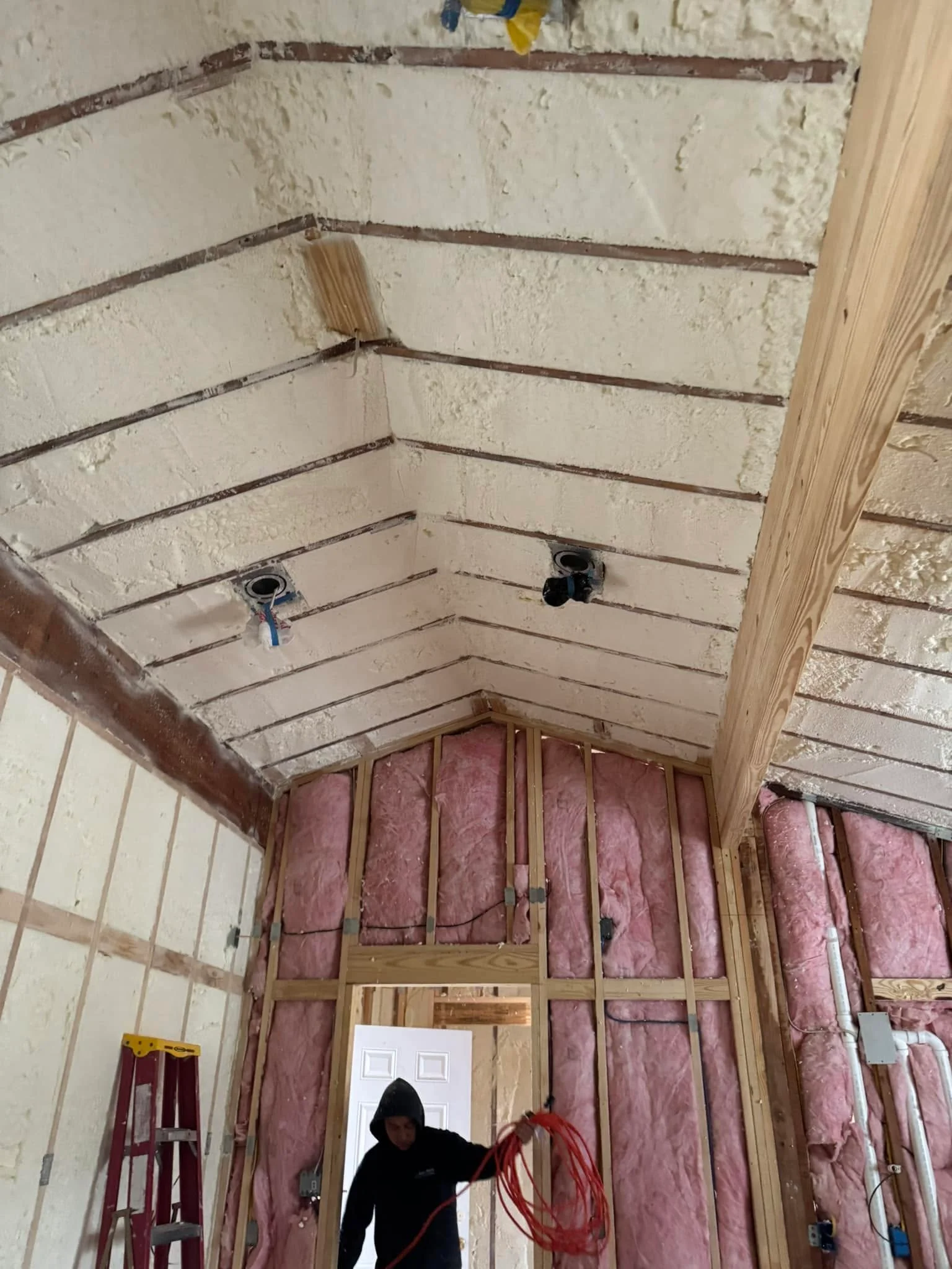Vaulted ceiling with spray foam insulation alongside wall studs filled with pink fiberglass insulation Insulation Services in Salisbury, MD